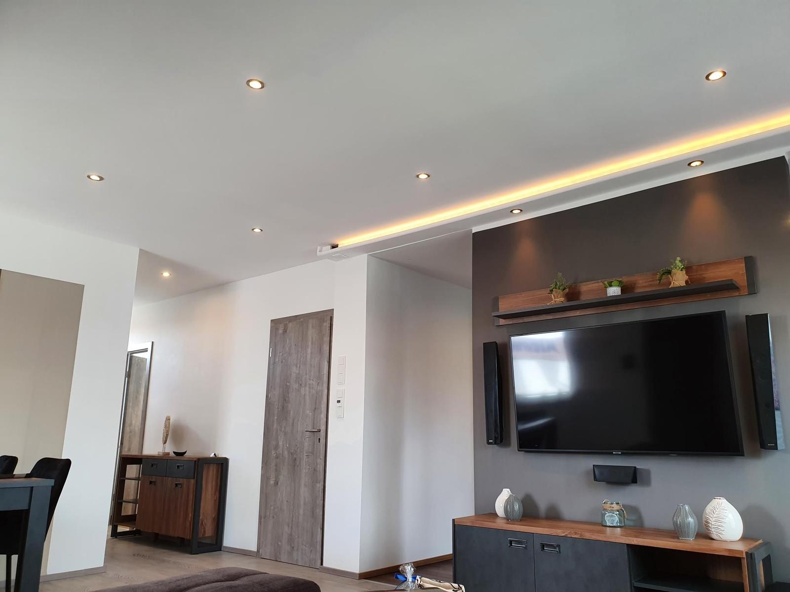 Wohnzimmer mit Fernseher, Sideboard und Beleuchtung.