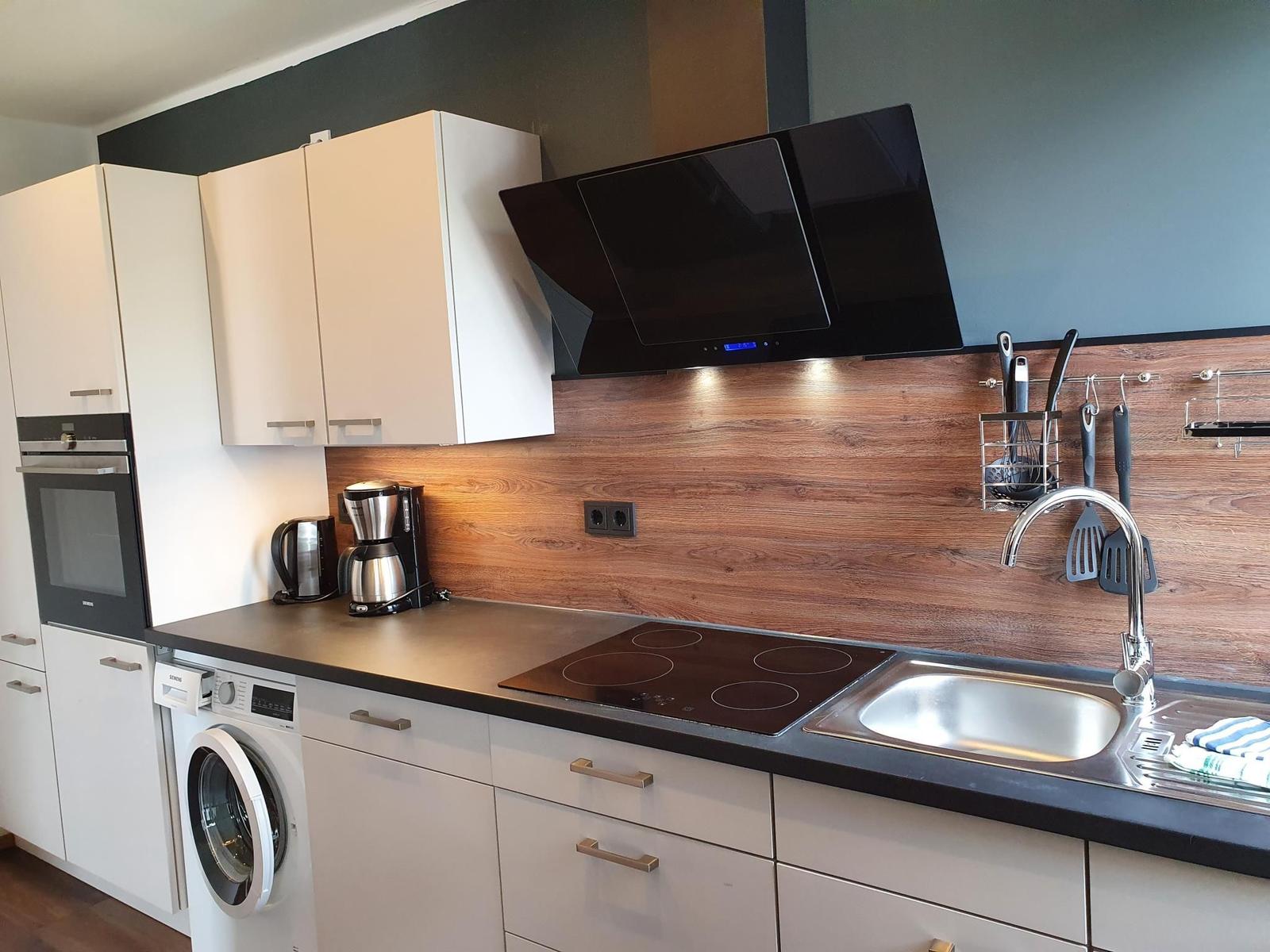 Küche mit Kochfeld, Spüle, Dunstabzug und Waschmaschine.