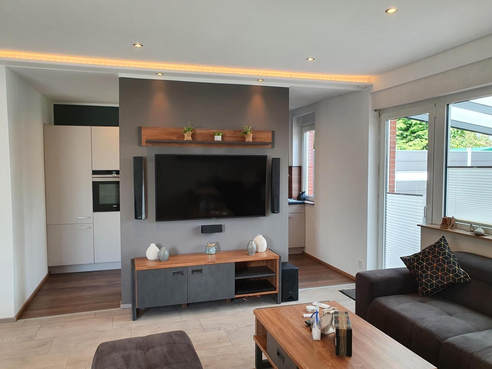 Wohnzimmer mit TV, Sofa und Küchenbereich im Hintergrund.