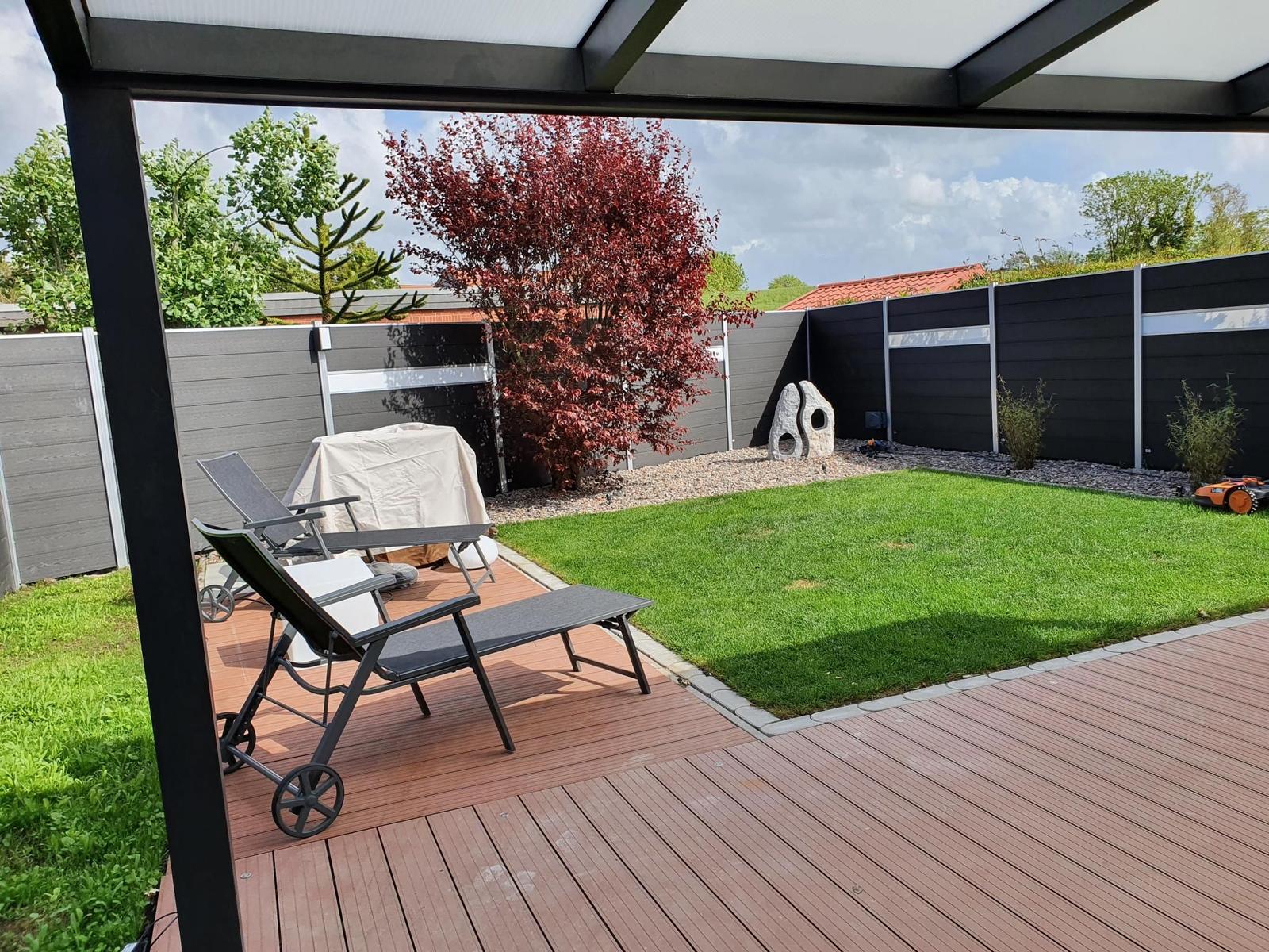 Terrasse mit Liegestühlen und Grünfläche hinter Schutzwand.
