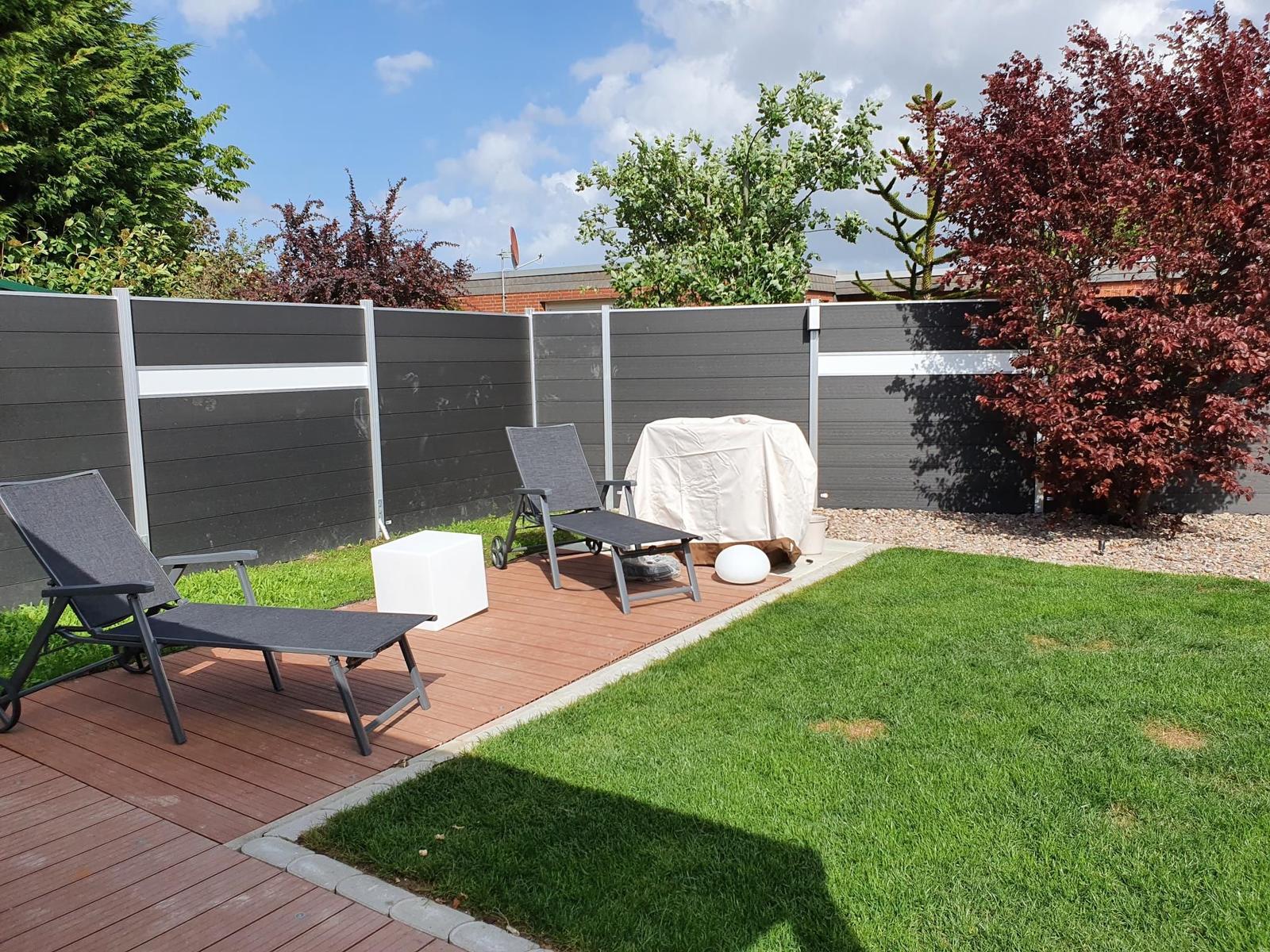 Hinterhof mit Terrasse, Liegestühlen und Rasenfläche.
