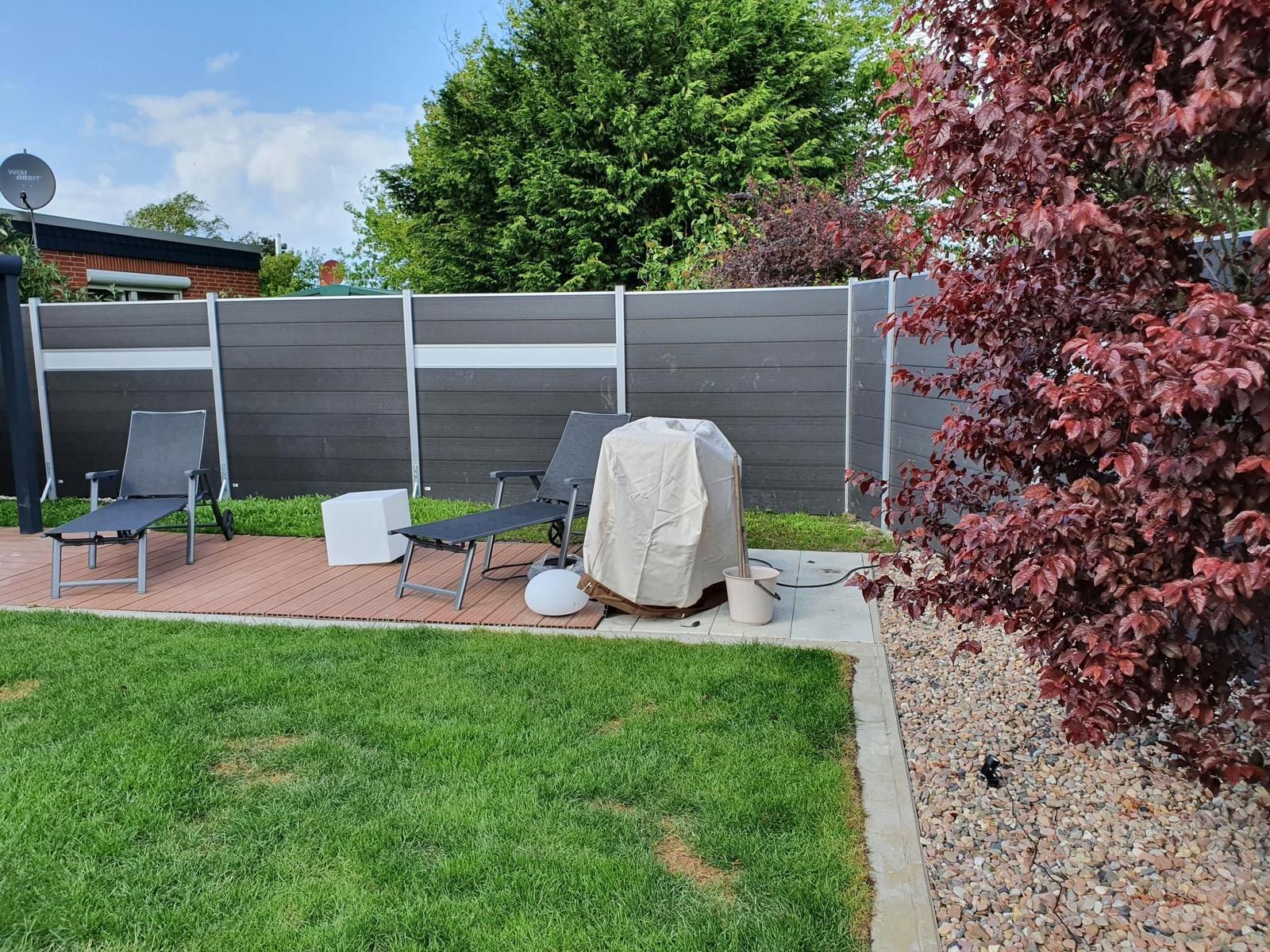 Hinterhof mit Garten, Terrasse und Liegestühlen. Grill und Pflanzen sind vorhanden.