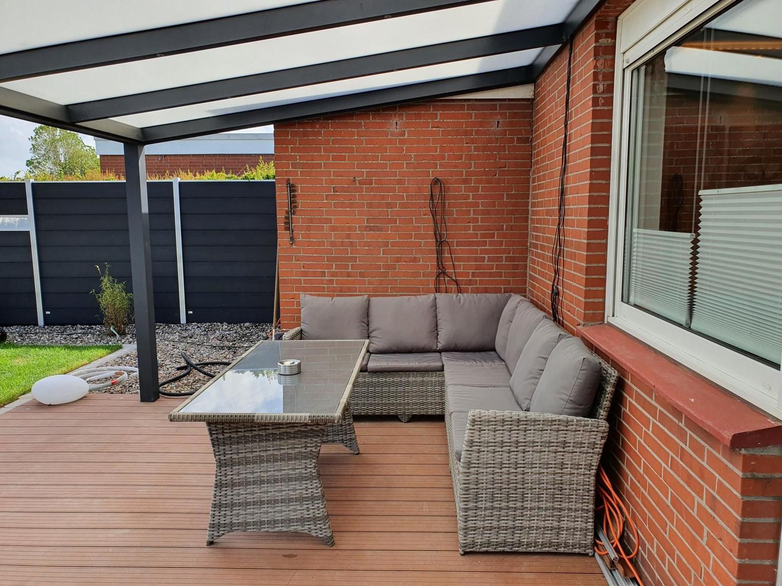 Terrasse mit Sitzgruppe, Glas-Tisch und Dachüberdachung an roter Ziegelwand.