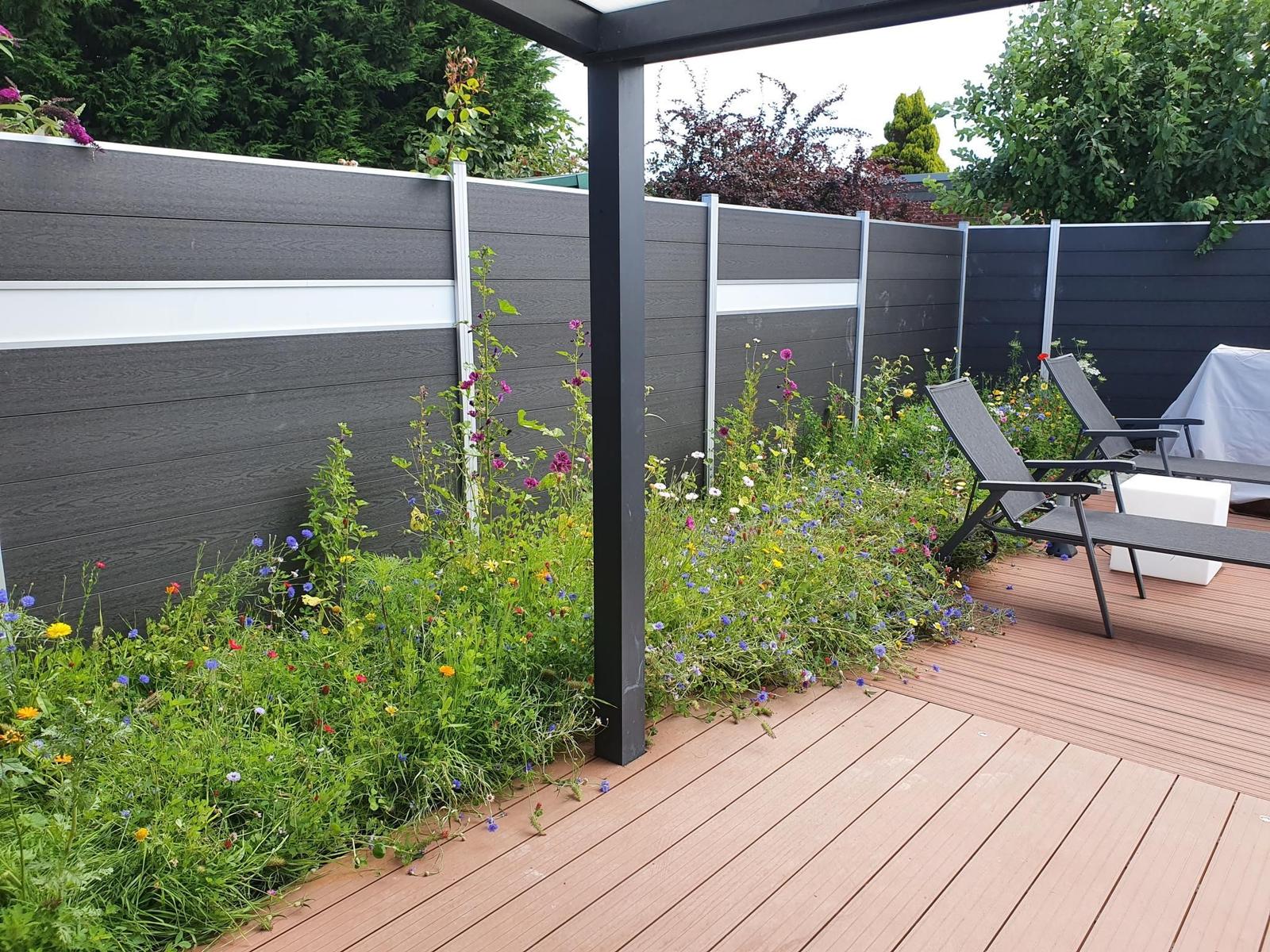 Terrasse mit Liegestühlen und Blumenbeet an grauer Holzumzäunung.