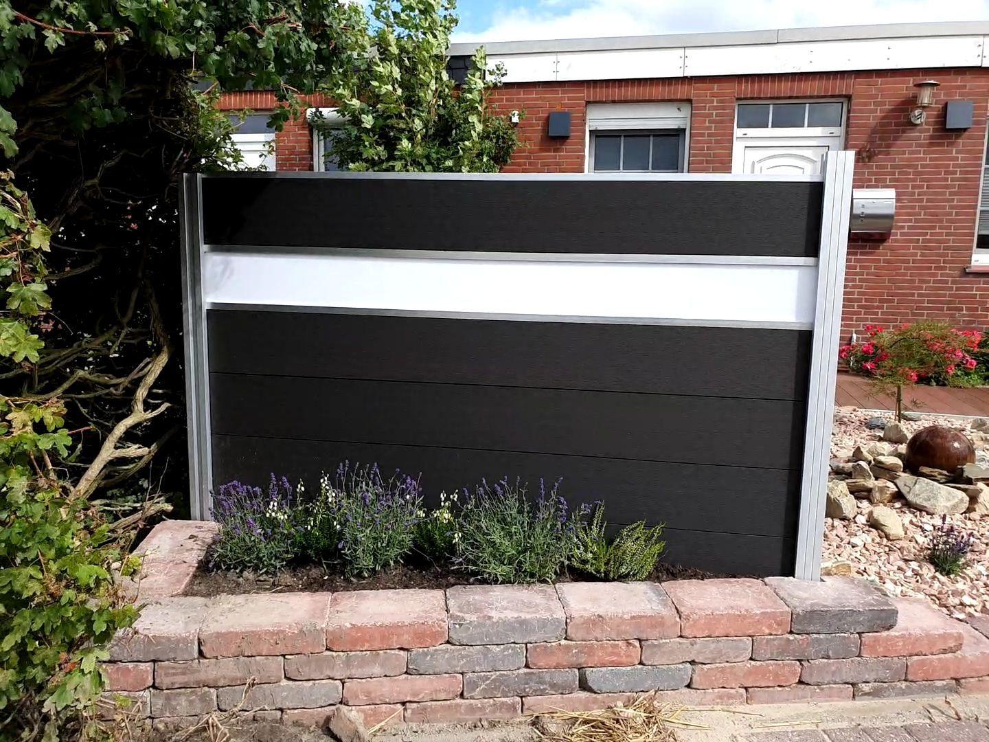 Moderne schwarze und weiße Sichtschutzwand vor einem Backsteinhaus mit Beet und Steinmauer.