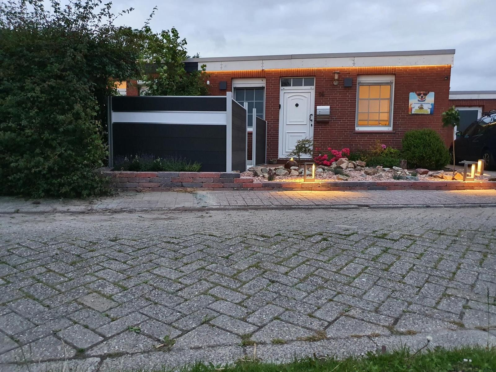 Einfamilienhaus mit Garten, Beleuchtung und gepflastertem Vorplatz.