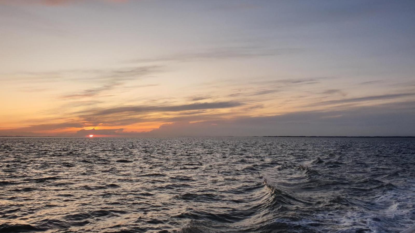 Sonnenuntergang über dem Meer mit Wellen und farbigen Wolken am Horizont.