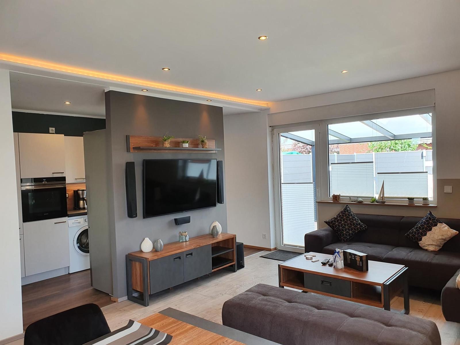 Wohnbereich mit Sofa, TV und Küche im Hintergrund.