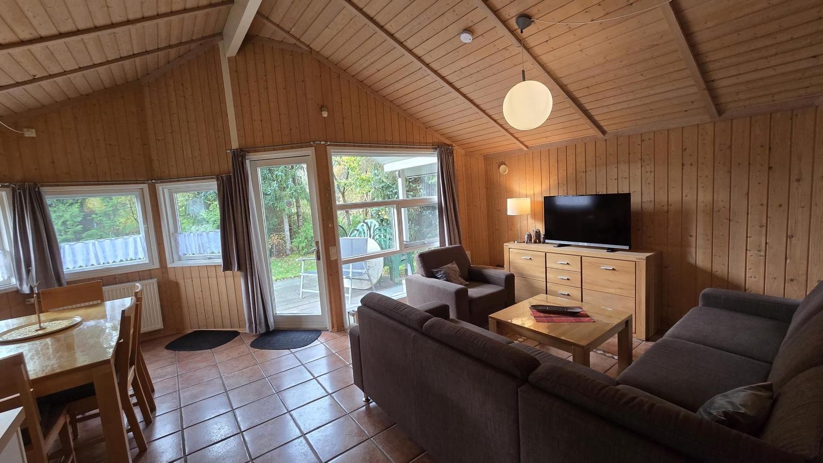 Wohn- und Essbereich mit Holzwand, Sofa, TV und Terrassentür.