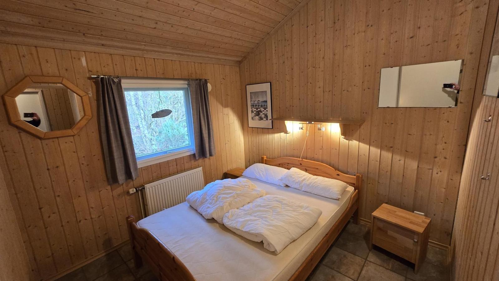 Schlafzimmer mit Holzwand, Bett, Fenster und Spiegeln.