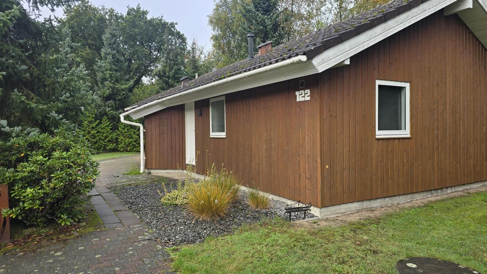 Holzhaus mit Nummer 122, Garten und Wald im Hintergrund.