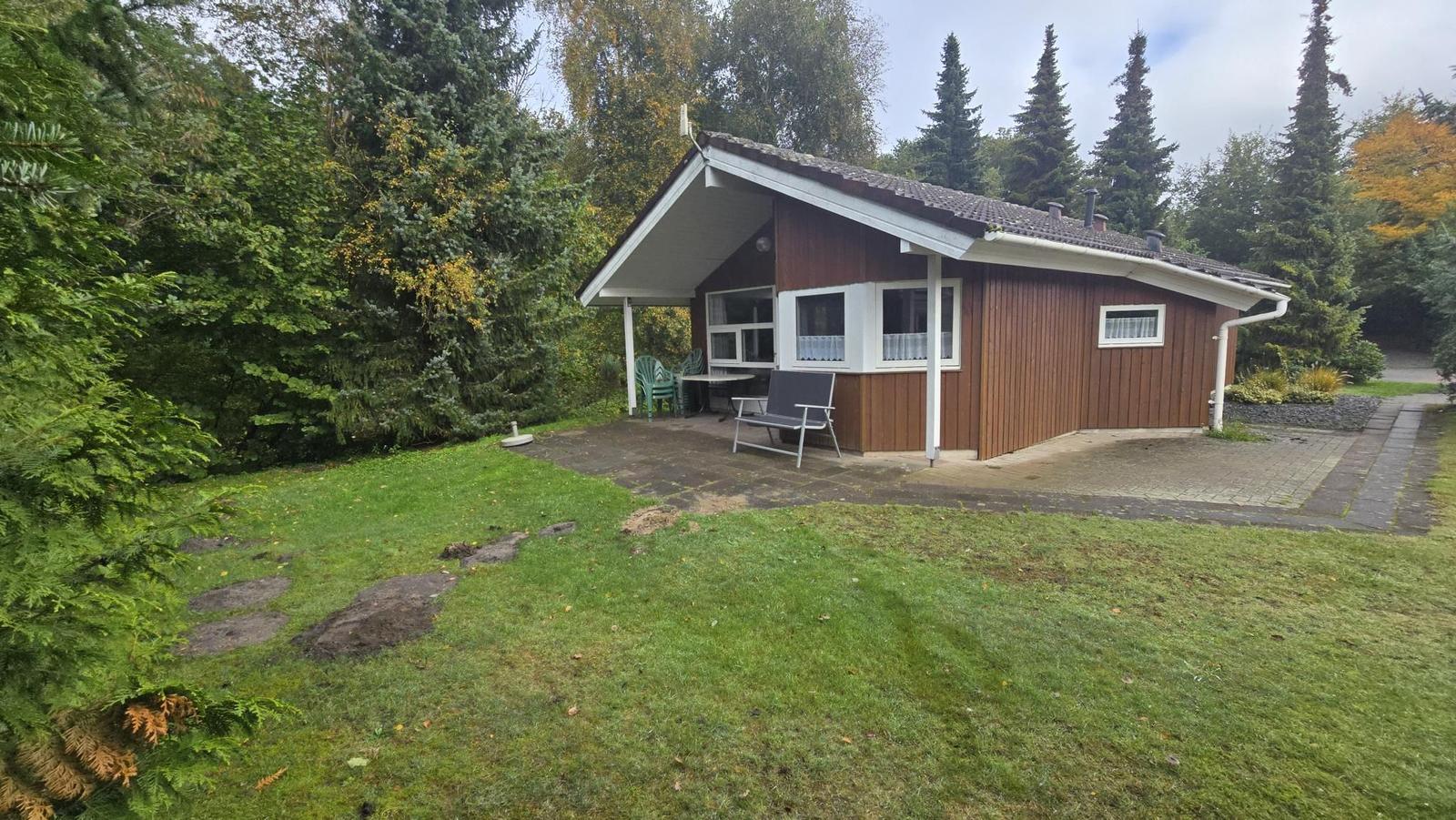 Holzhaus mit Terrasse, Garten und Bäumen im Hintergrund.