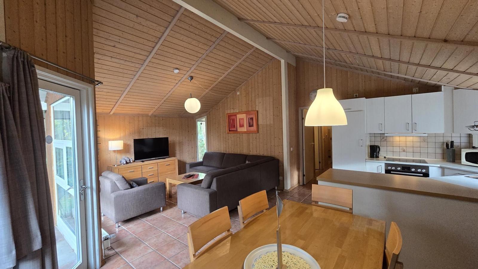 Wohnküche mit Holzdecke, Sofa, Esstisch und Küchenspüle