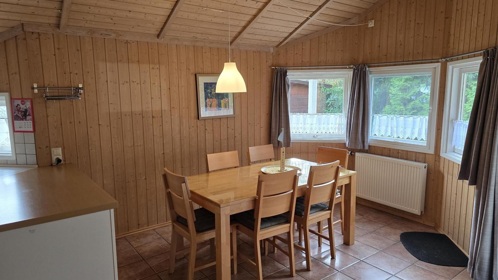 Essbereich mit Holztisch, sechs Stühlen und Fenstern mit Blick nach draußen.