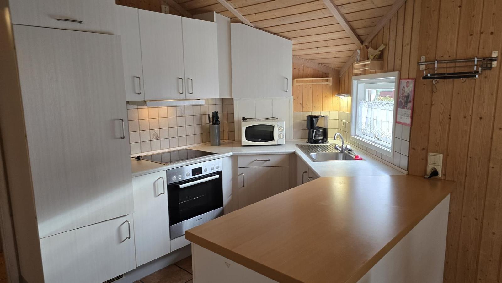 Küche mit weißen Schränken, Herd und Spüle. Holzwände und Dach.
