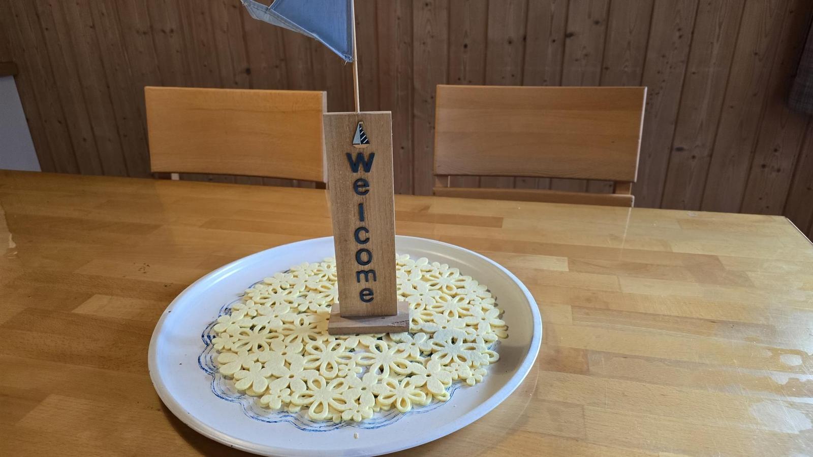 Willkommen-Schild mit Segelboot auf Teller mit Blumenkuchen