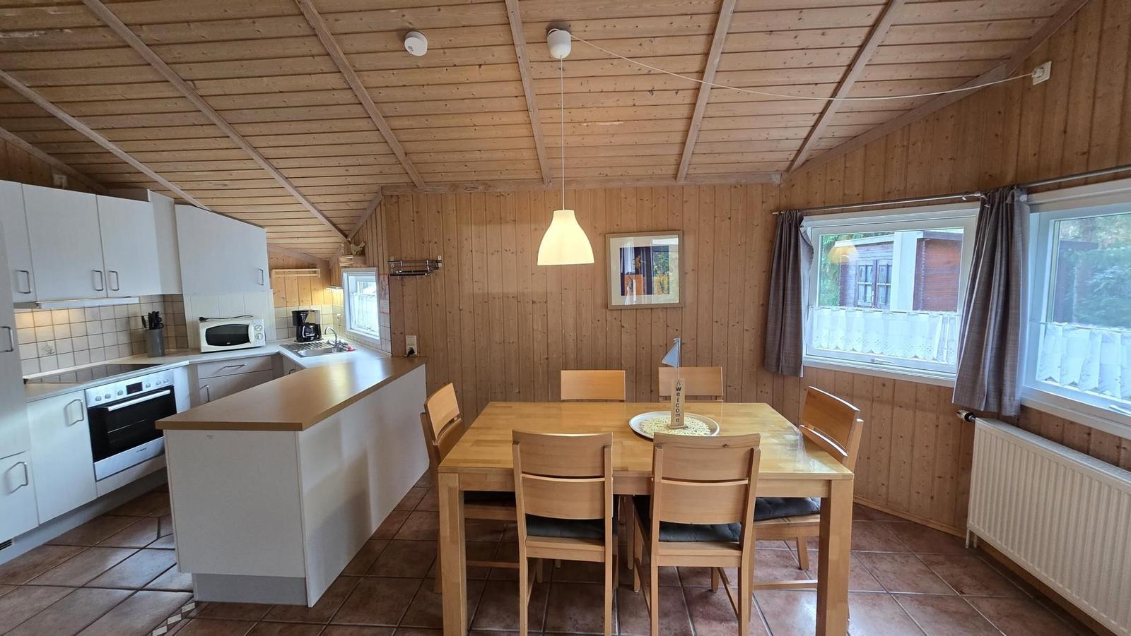 Küche und Essbereich mit Holzwänden und -decke. Esstisch mit sechs Stühlen.