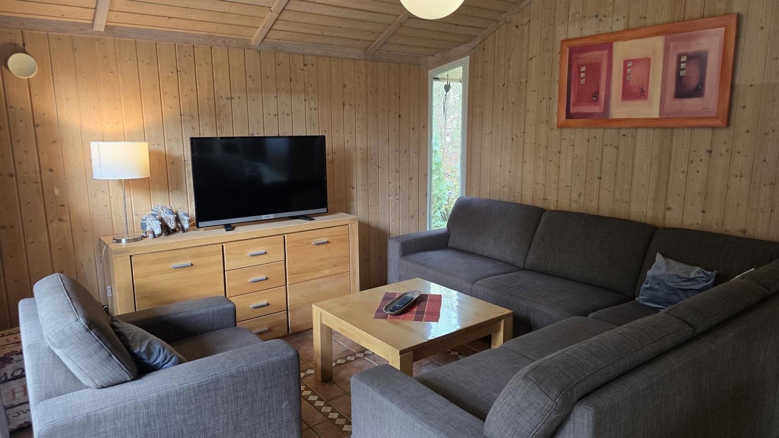 Wohnzimmer mit Sofa, Sessel, Fernseher und Holzmöbel.
