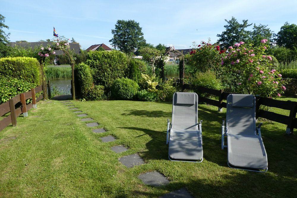 Zwei Liegestühle stehen auf einer grünen Wiese neben einem Gartenzaun und blühenden Rosen.