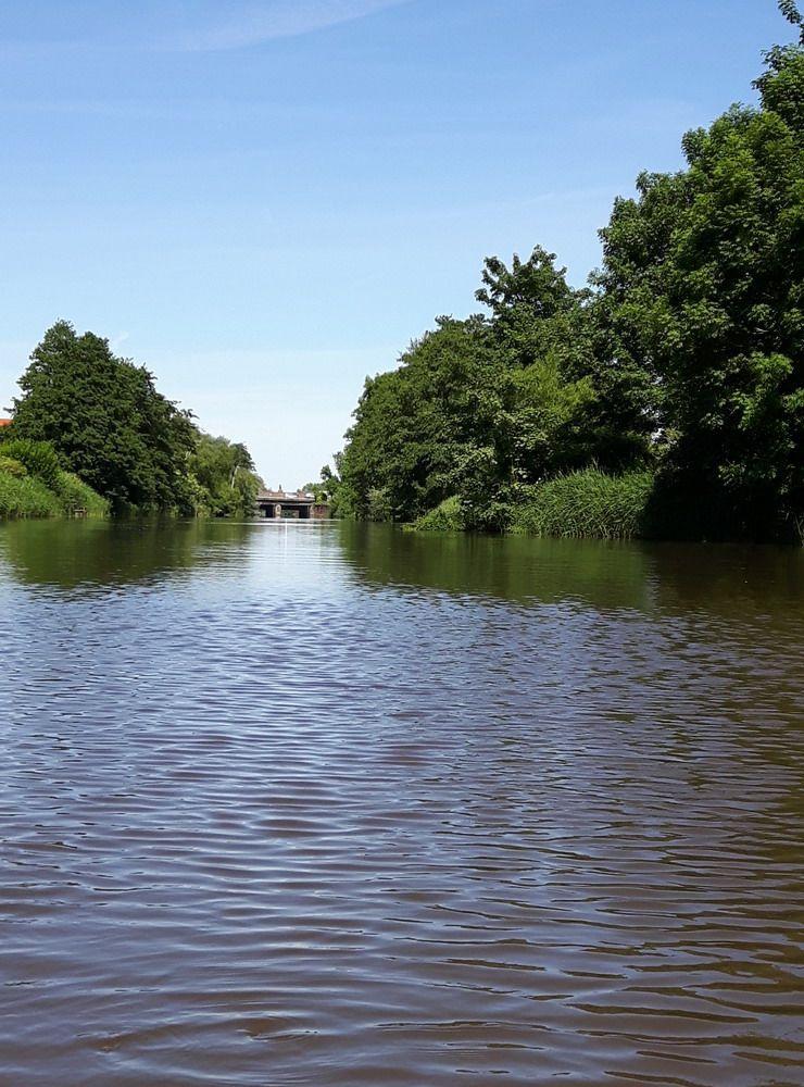 Ein ruhiger Kanal mit Bäumen und einem Brückenbau im Hintergrund.