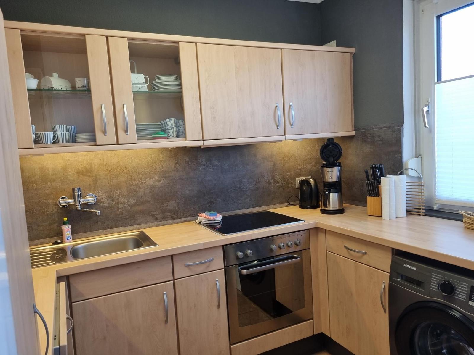 Küche mit Holzschränken, Spüle, Herd und Waschmaschine