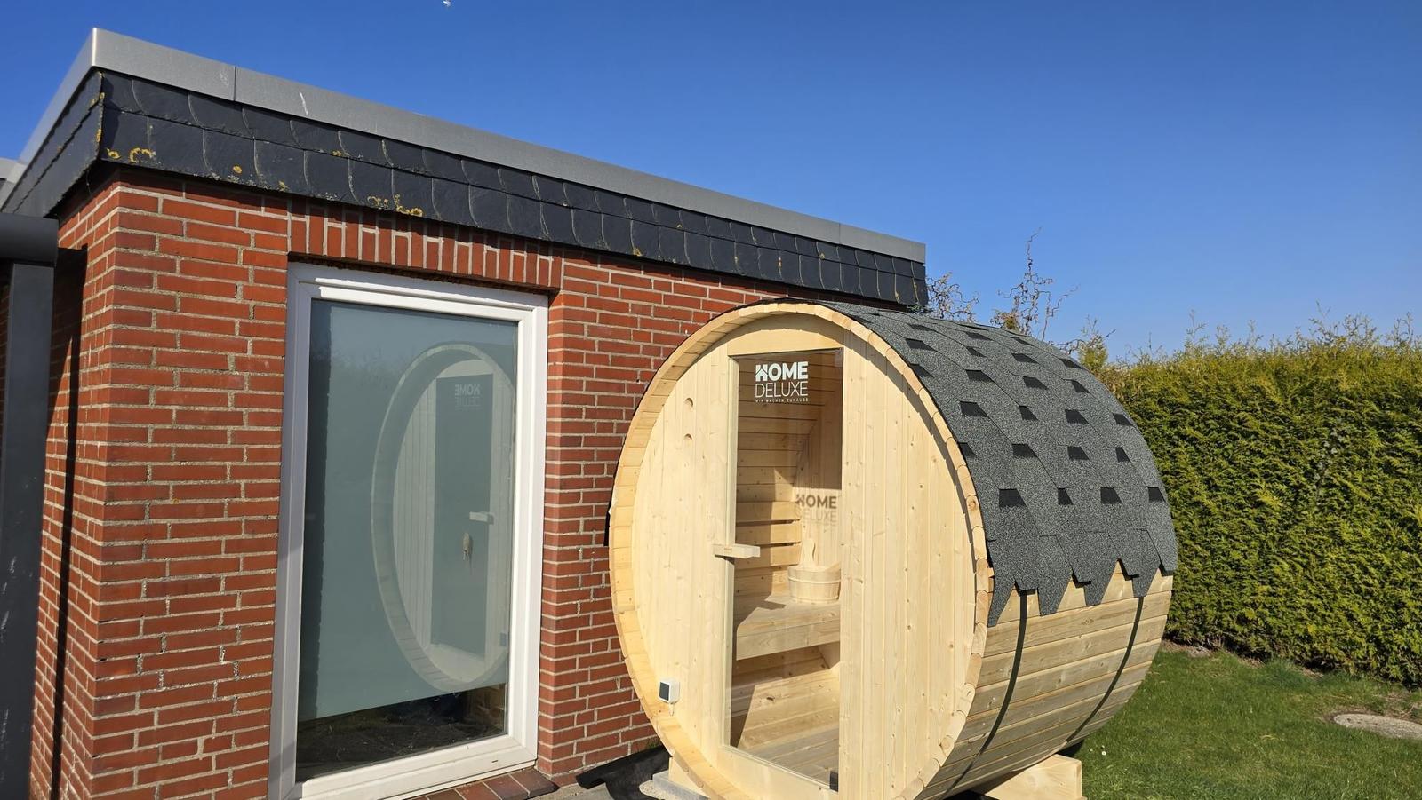 Holzsauna mit Dach und Sitzbänken an einer Backsteinmauer.