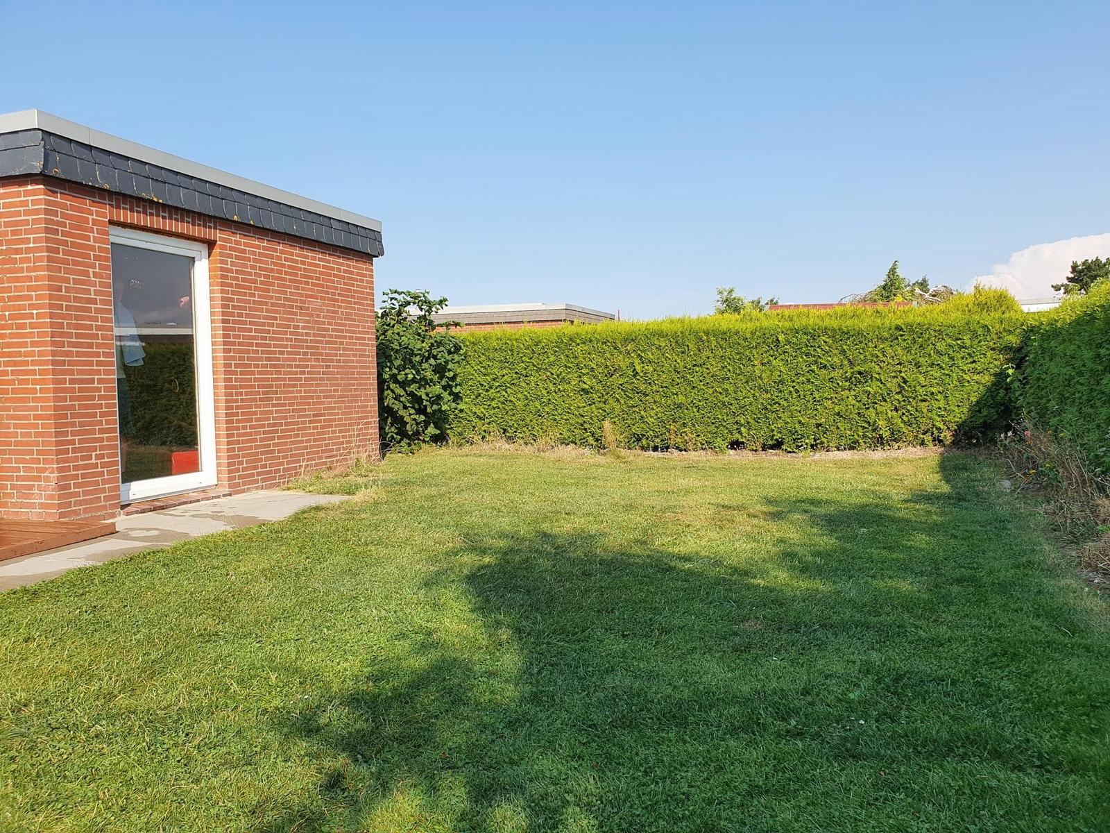 Roter Backsteinbau mit grünem Rasen und Hecke im Hintergrund.