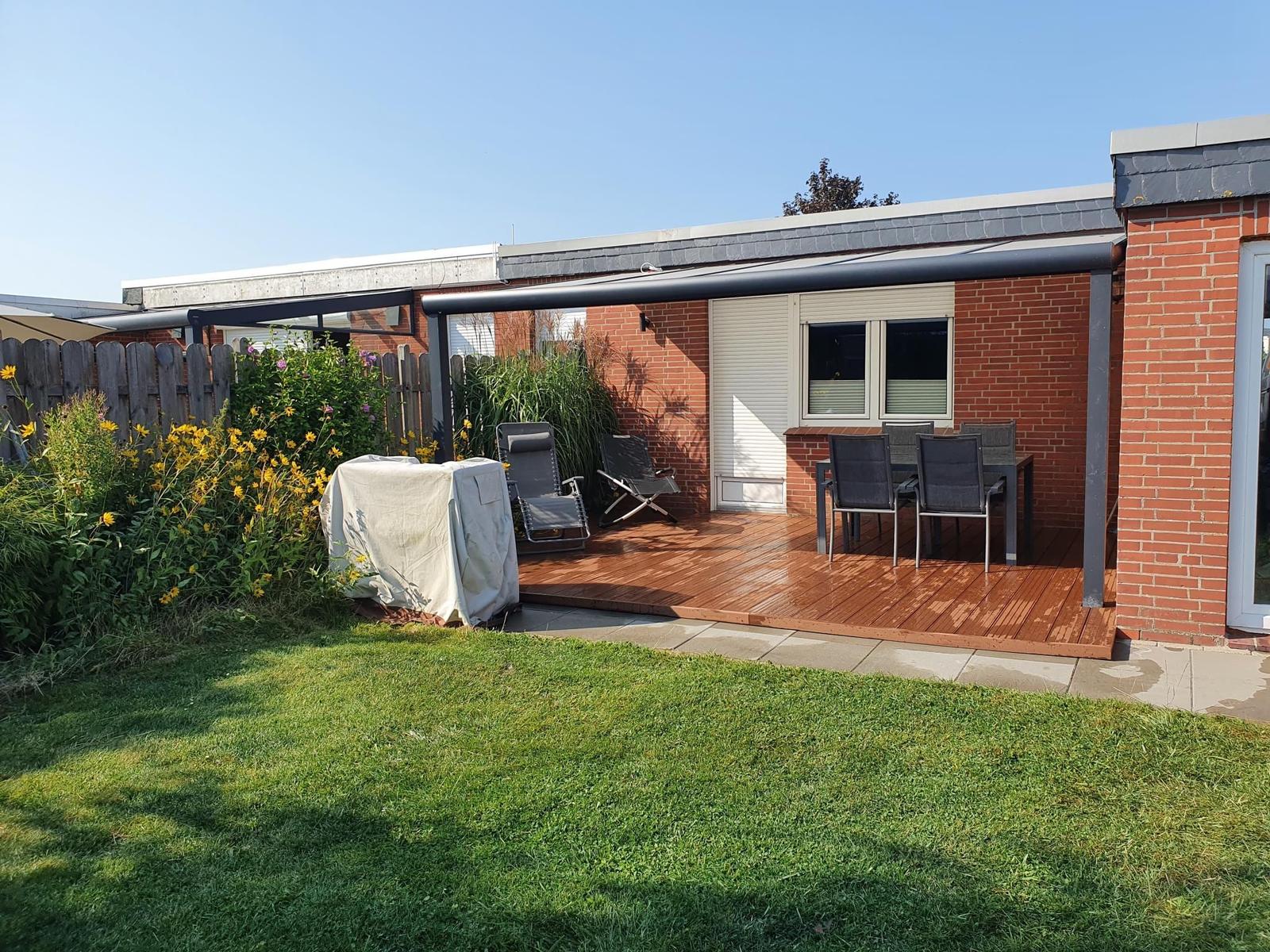 Terrasse mit Sitzgruppe, Garten und Grillplatz. Modernes Haus mit rotem Backsteinmauerwerk.