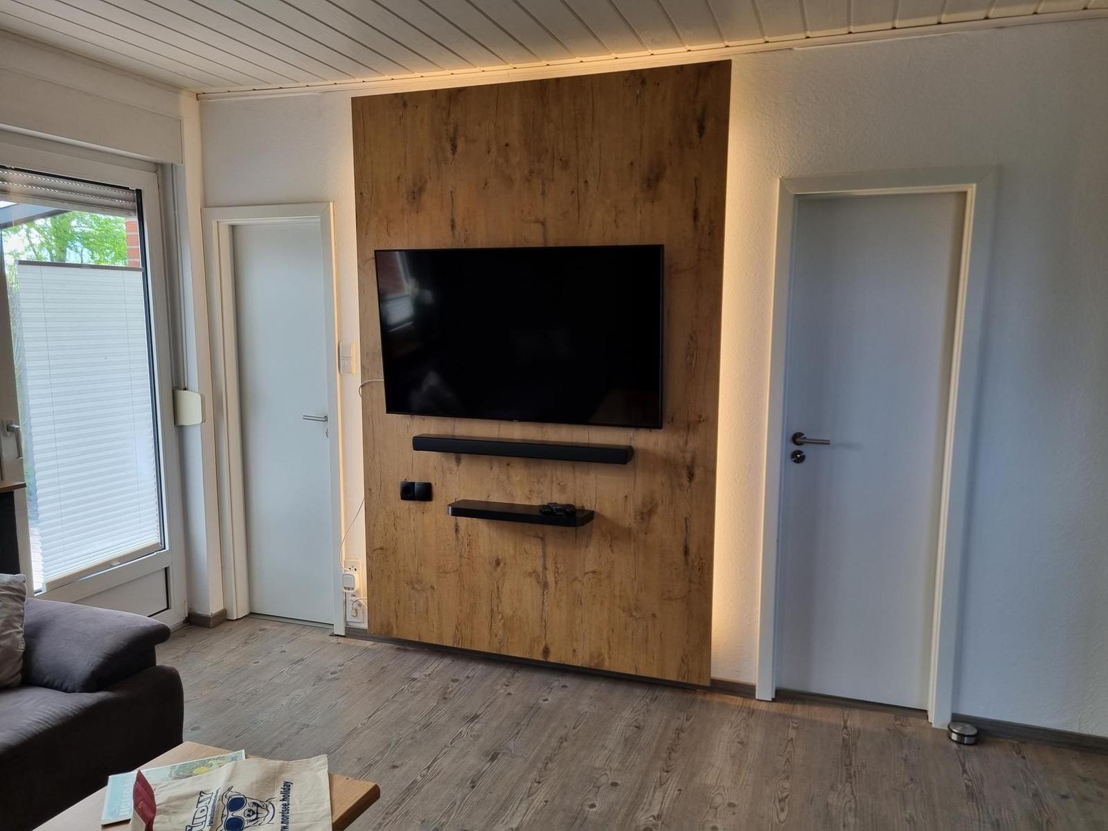 Wohnzimmer mit TV an Holzwand, Tür und Fenster.
