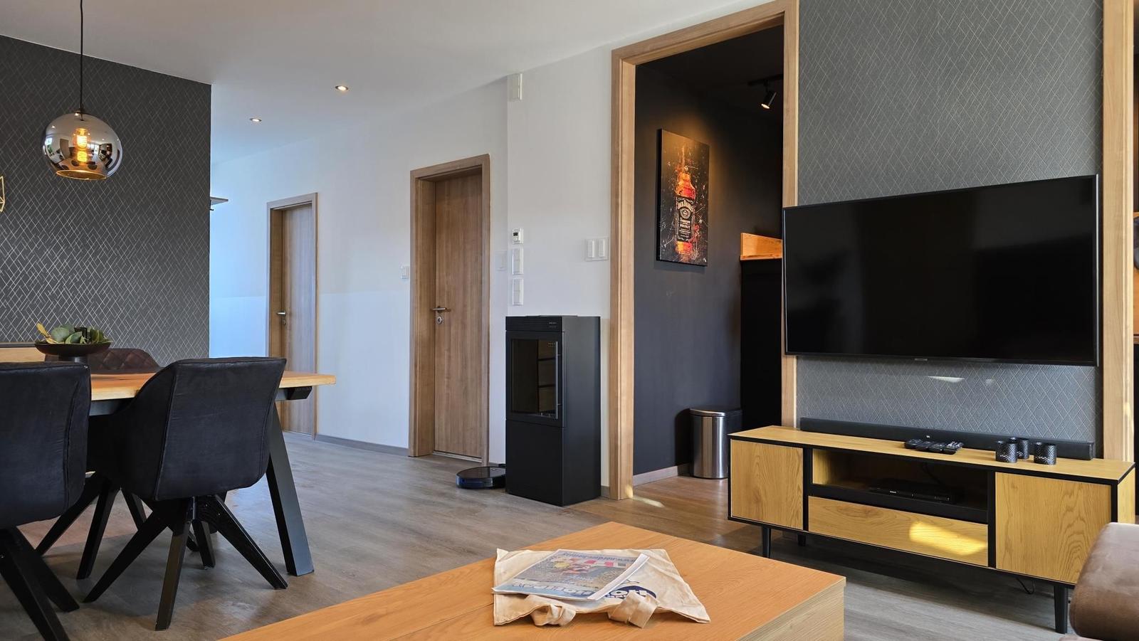 Wohn- und Essbereich mit Fernseher, Tisch und Stühlen sowie Tür zu einem anderen Raum.