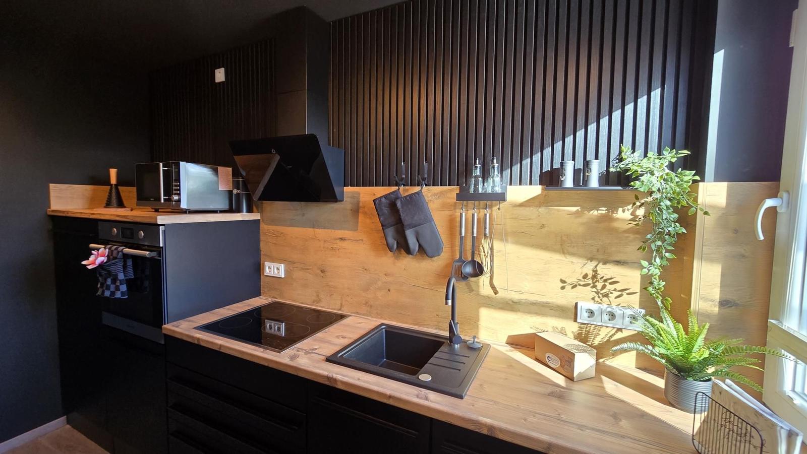 Küche mit Holzoberflächen, Herd, Spüle und Pflanzen an Fenster.