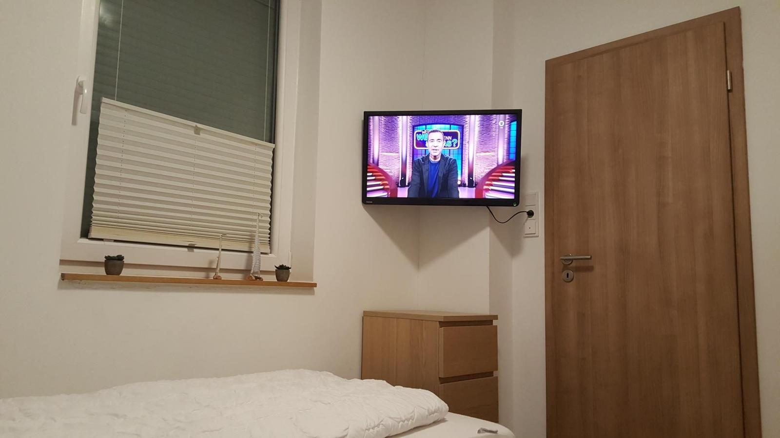 Schlafzimmer mit Bett, TV und Fenster mit Jalousie.