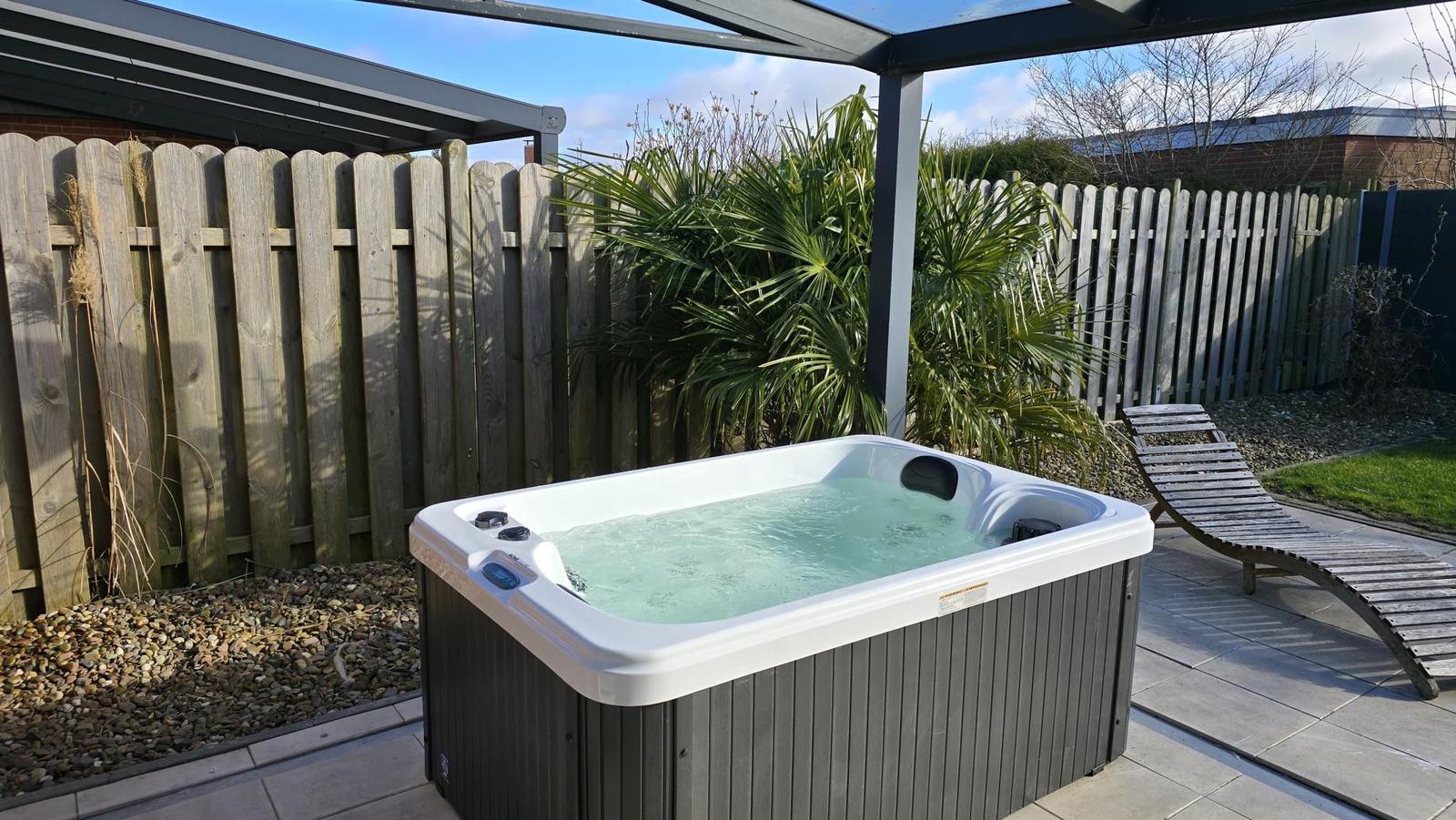 Hochwertige Whirlpool-Badewanne im Garten unter Pavillon mit Liege und Pflanzen.