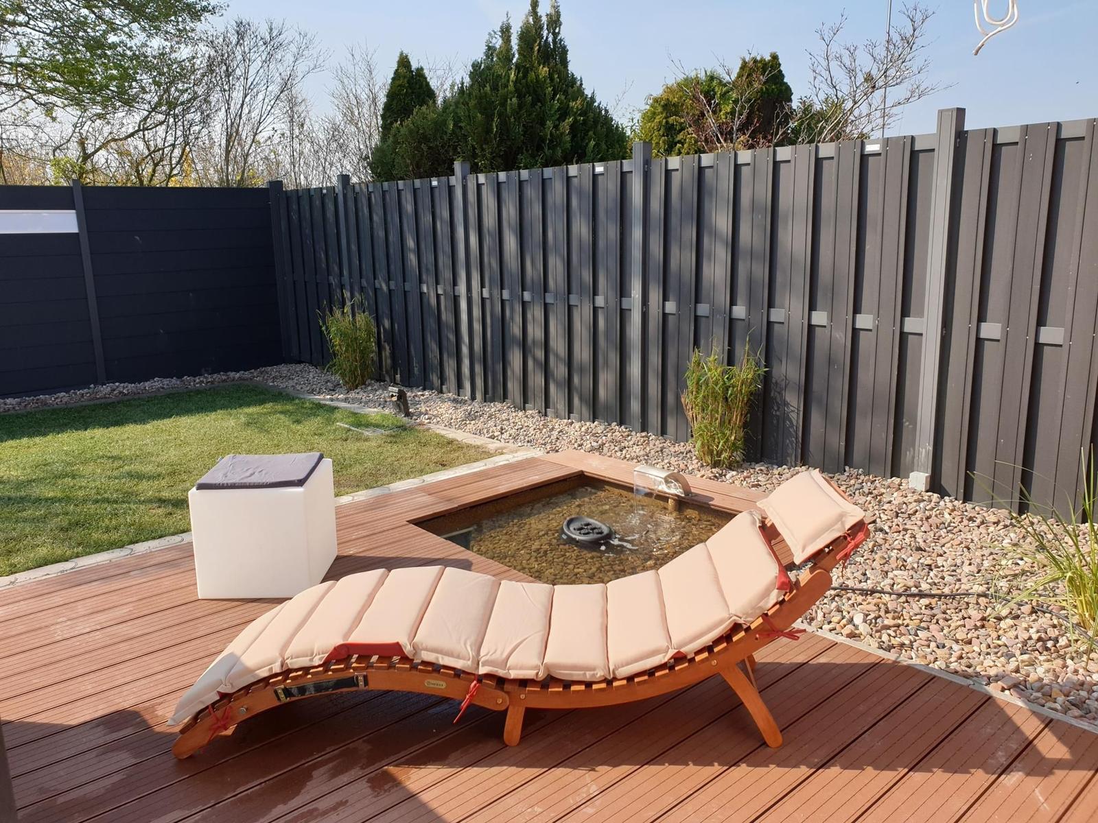 Holzliege mit Kissen neben einem kleinen Pool auf einer Terrasse.