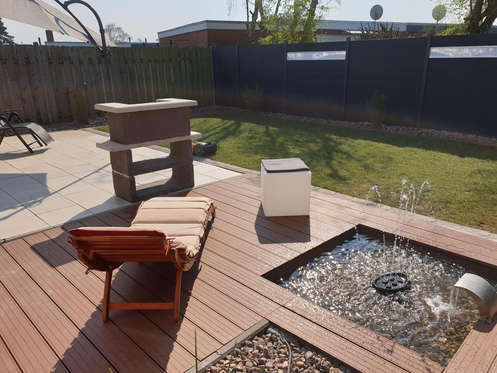 Terrasse mit Liege, Brunnen und Garten. Holzdecke und Rasenfläche.
