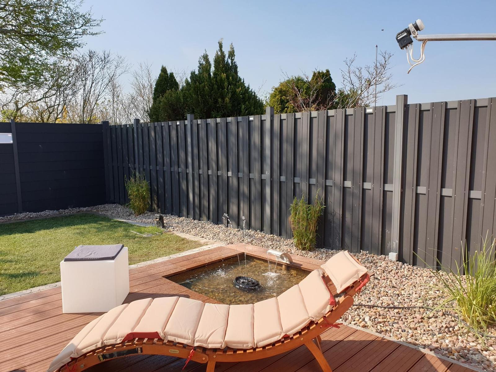 Hinterhof mit Liegestuhl, Brunnen und Holzterrasse.