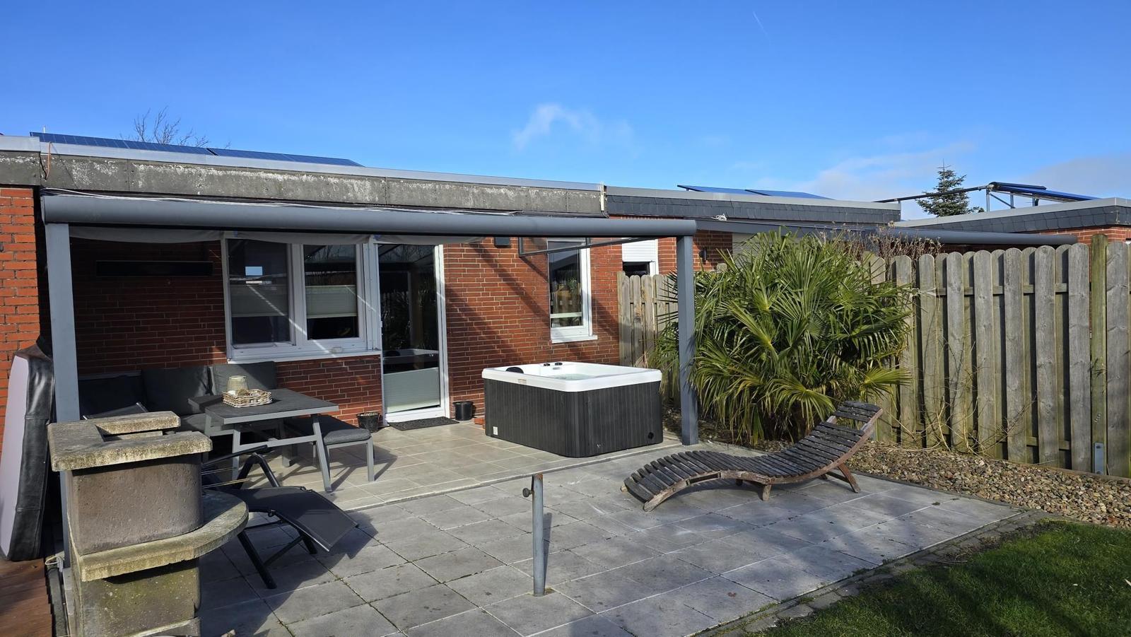 Terrasse mit Hot Tub, Loungebereich und Grillplatz. Holzzaun und Palme im Hintergrund.