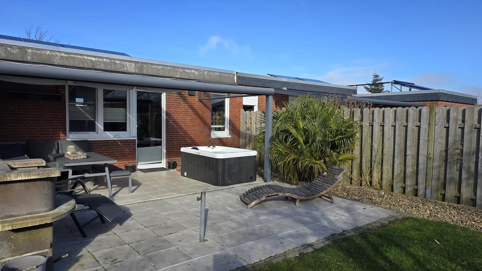 Terrasse mit Whirlpool, Sonnenliegen und Grillplatz. Hinterhof mit Holzzaun und Palme.