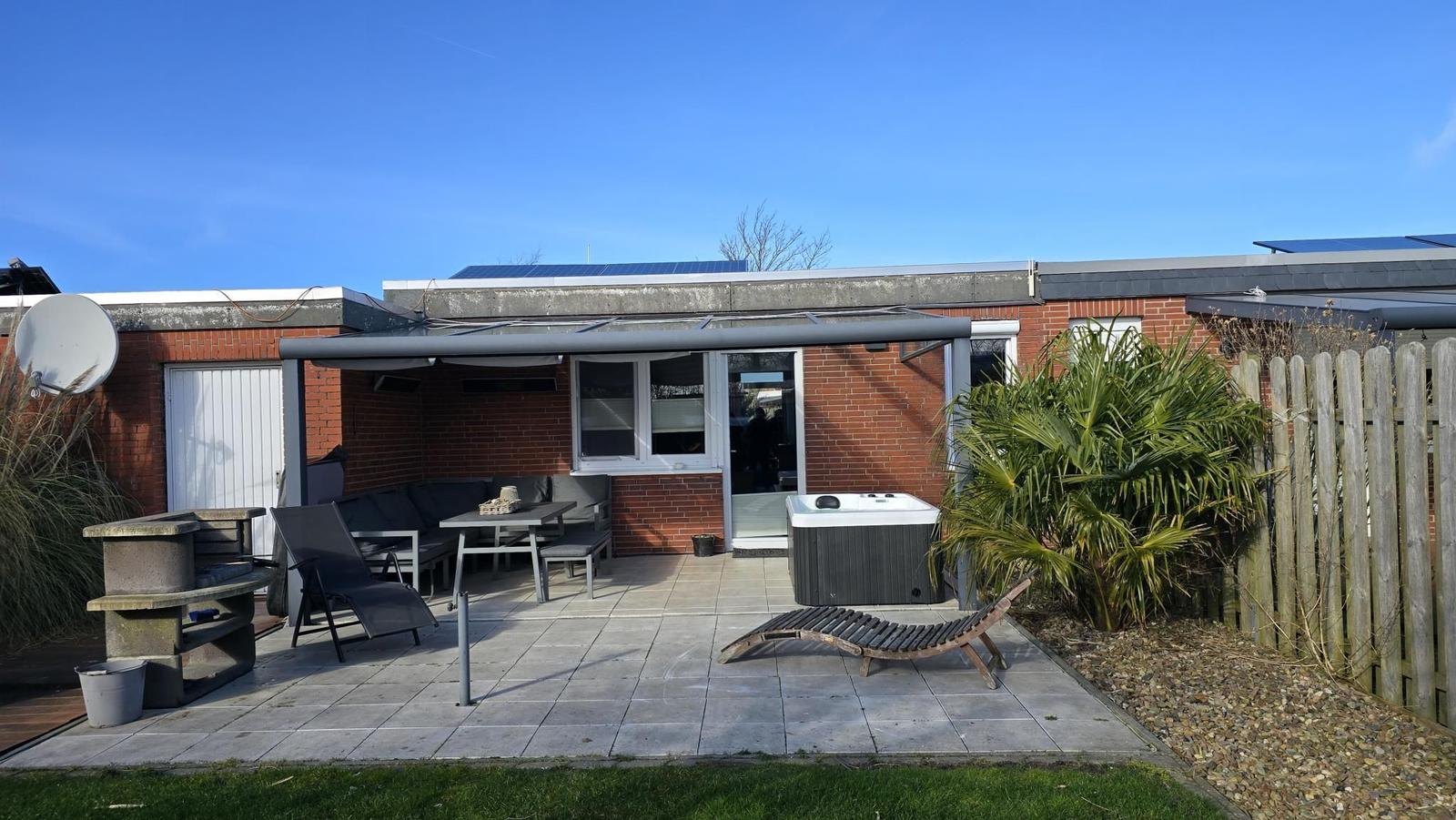 Terrasse mit Hot Tub, Sitzgruppe und Grillplatz. Garten mit Palme und Holzzaun.