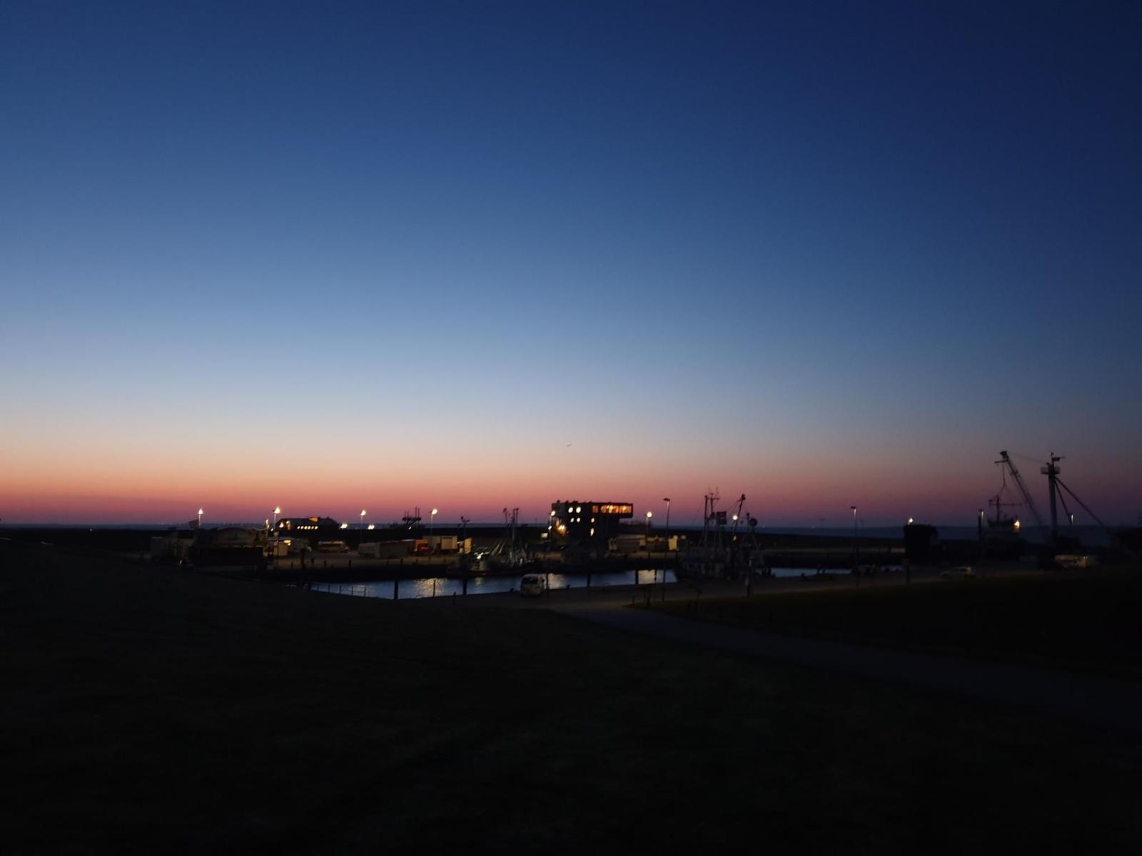 Hafen bei Dämmerung mit Schiffen und Kränen unter farbigem Himmel.