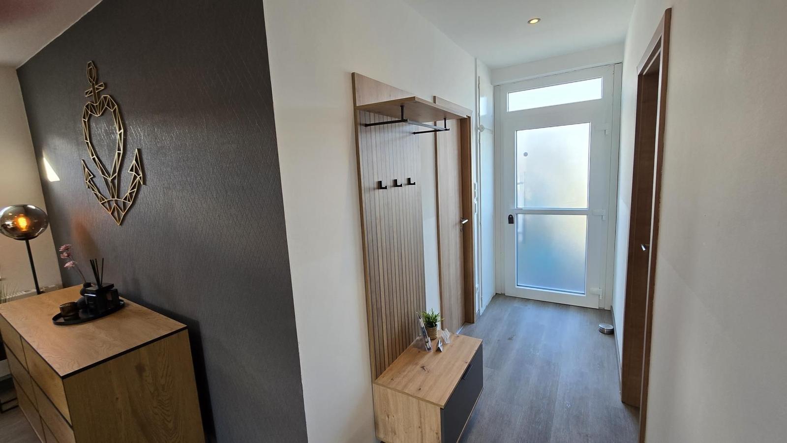 Eingangsbereich mit Garderobe, Holzregal und moderner Wanddekoration.