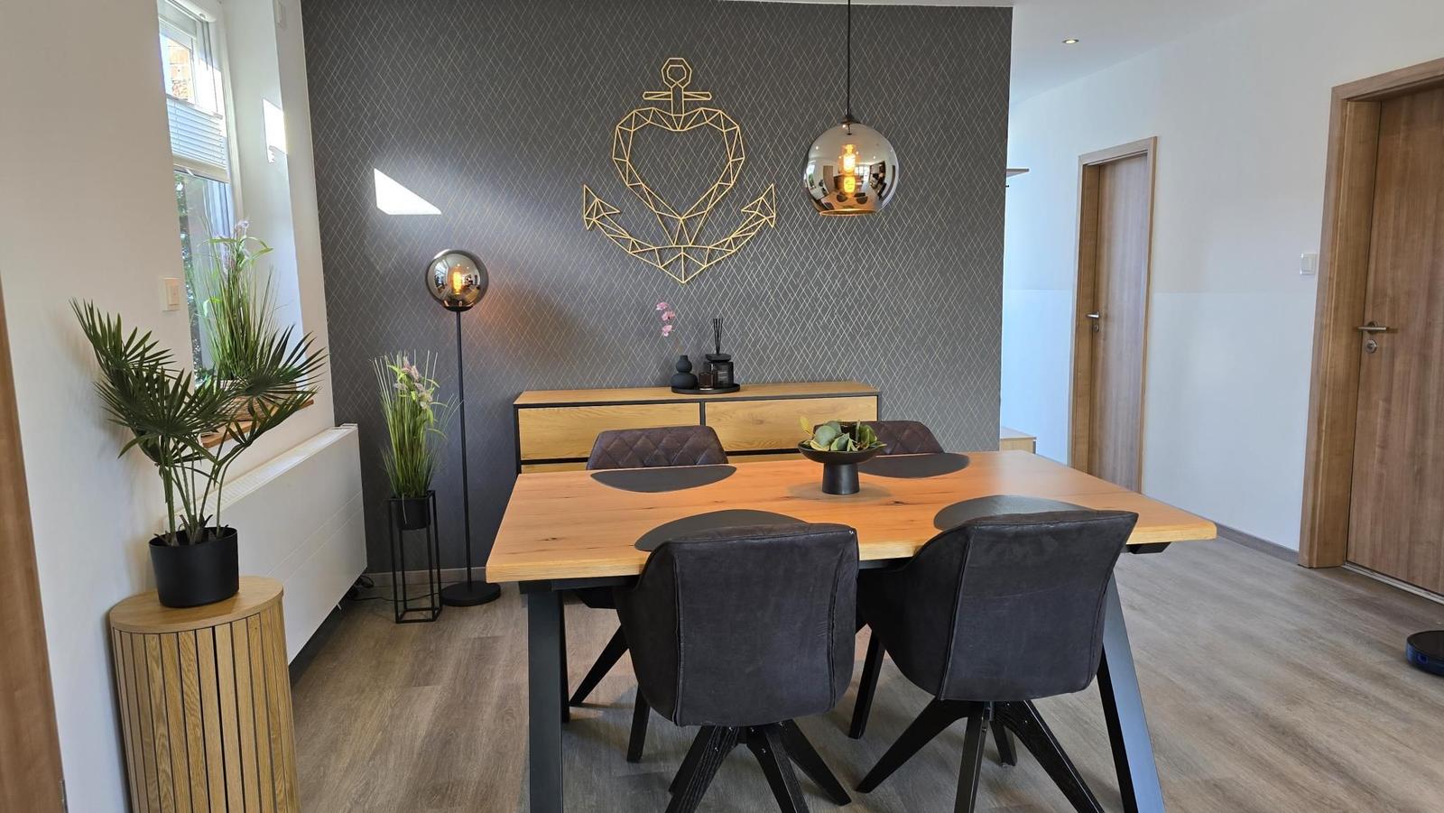 Esstisch mit vier Stühlen vor einer Wand mit Ankerdekoration.