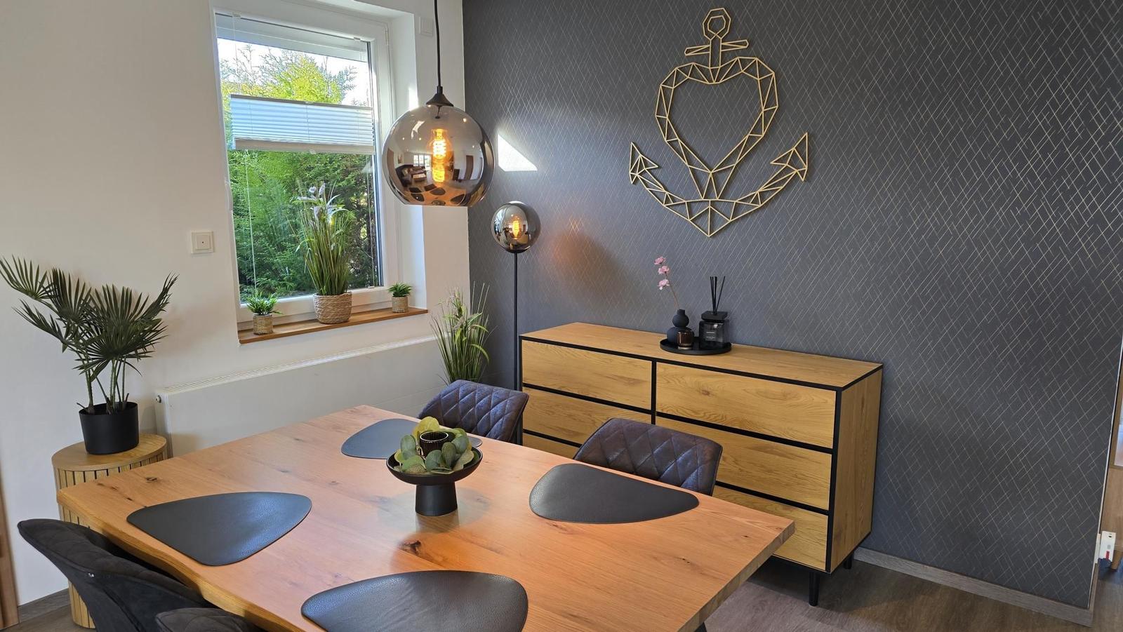 Esszimmer mit Holztisch, Stühlen und Pflanzen. Wanddekoration und Fensterblick.