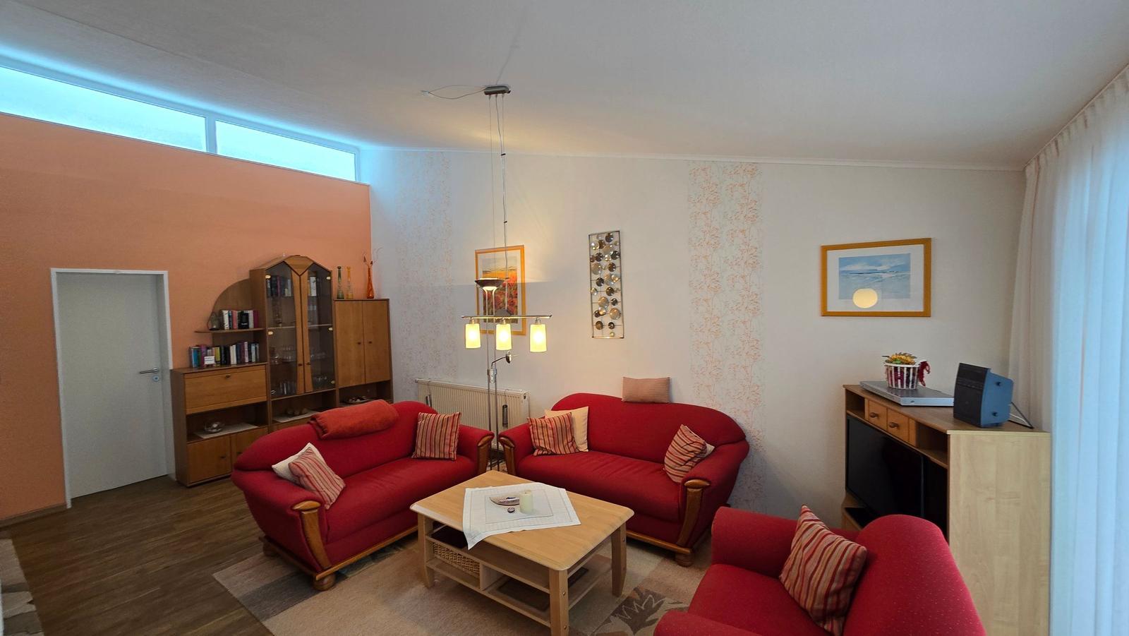 Wohnzimmer mit zwei roten Sofas, Couchtisch und Holzmöbeln.
