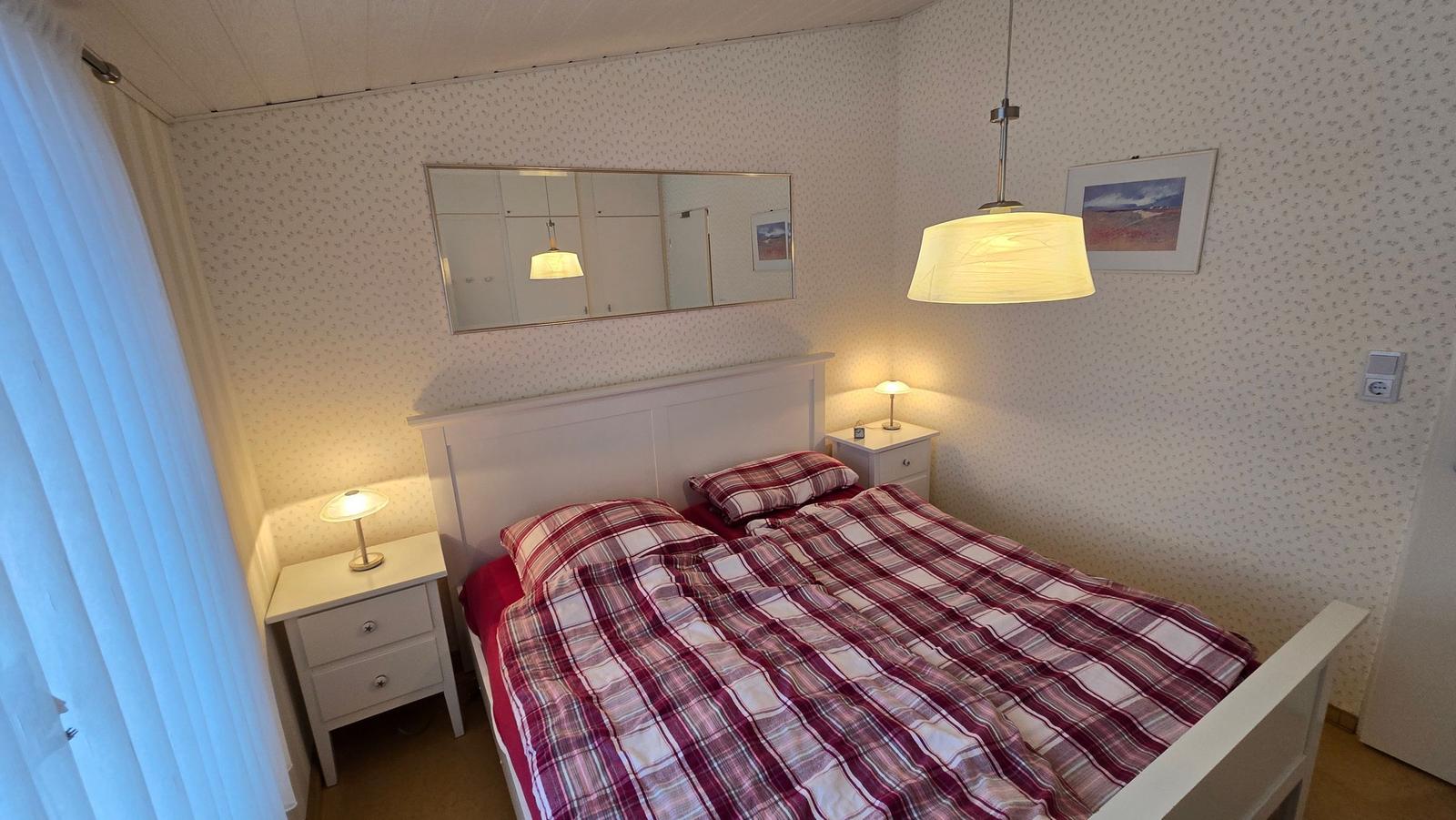 Schlafzimmer mit Bett, Nachttischen und Spiegel an der Wand.