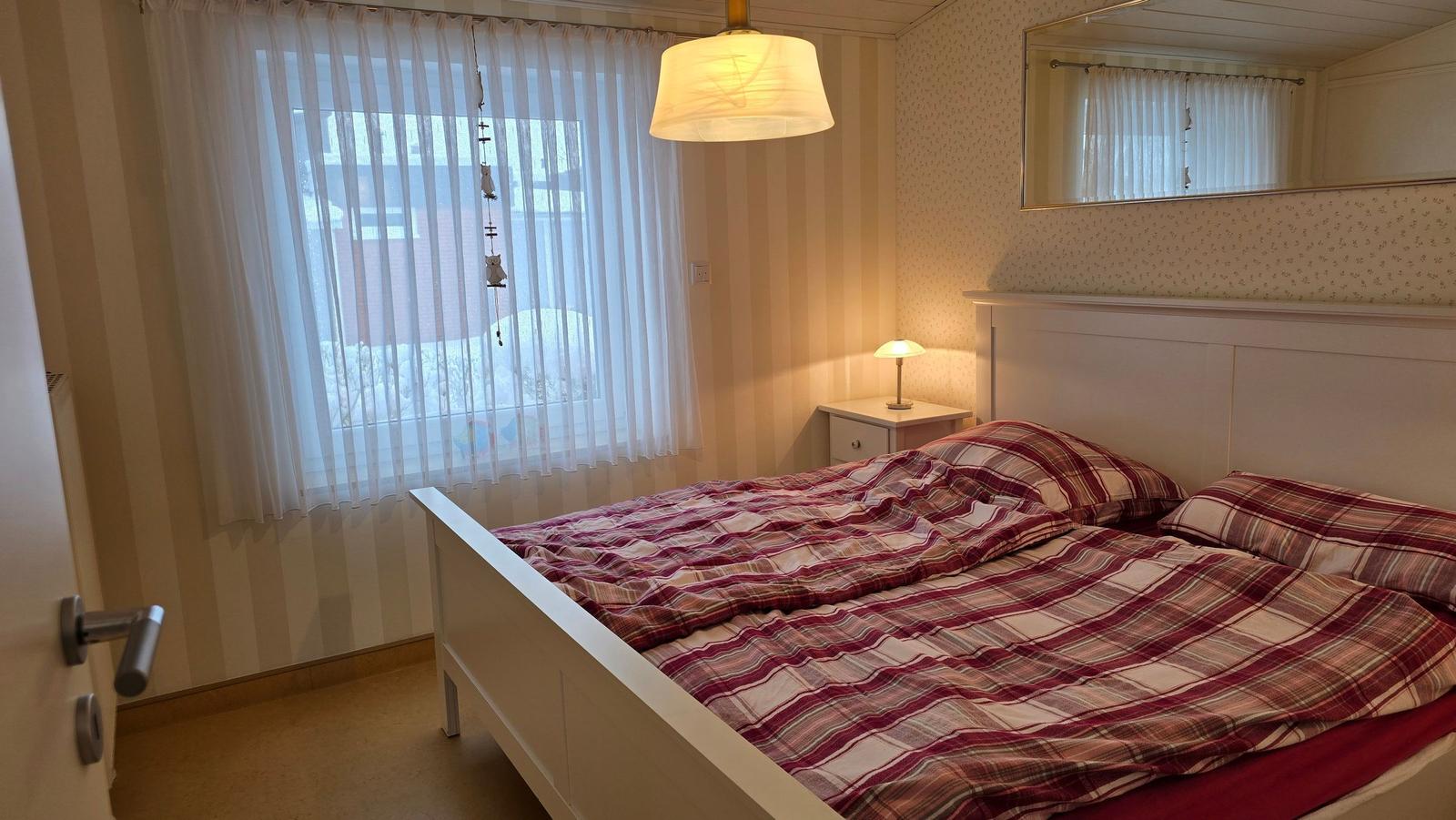Schlafzimmer mit Bett, Nachttisch und Fenster mit Vorhängen.