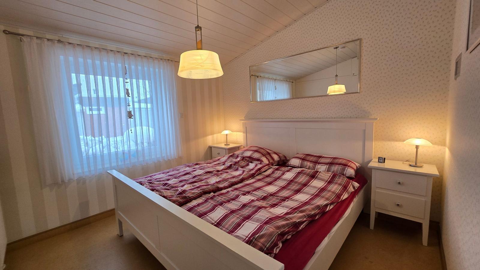 Schlafzimmer mit Doppelbett, zwei Nachttischen und Fenster mit Vorhängen.