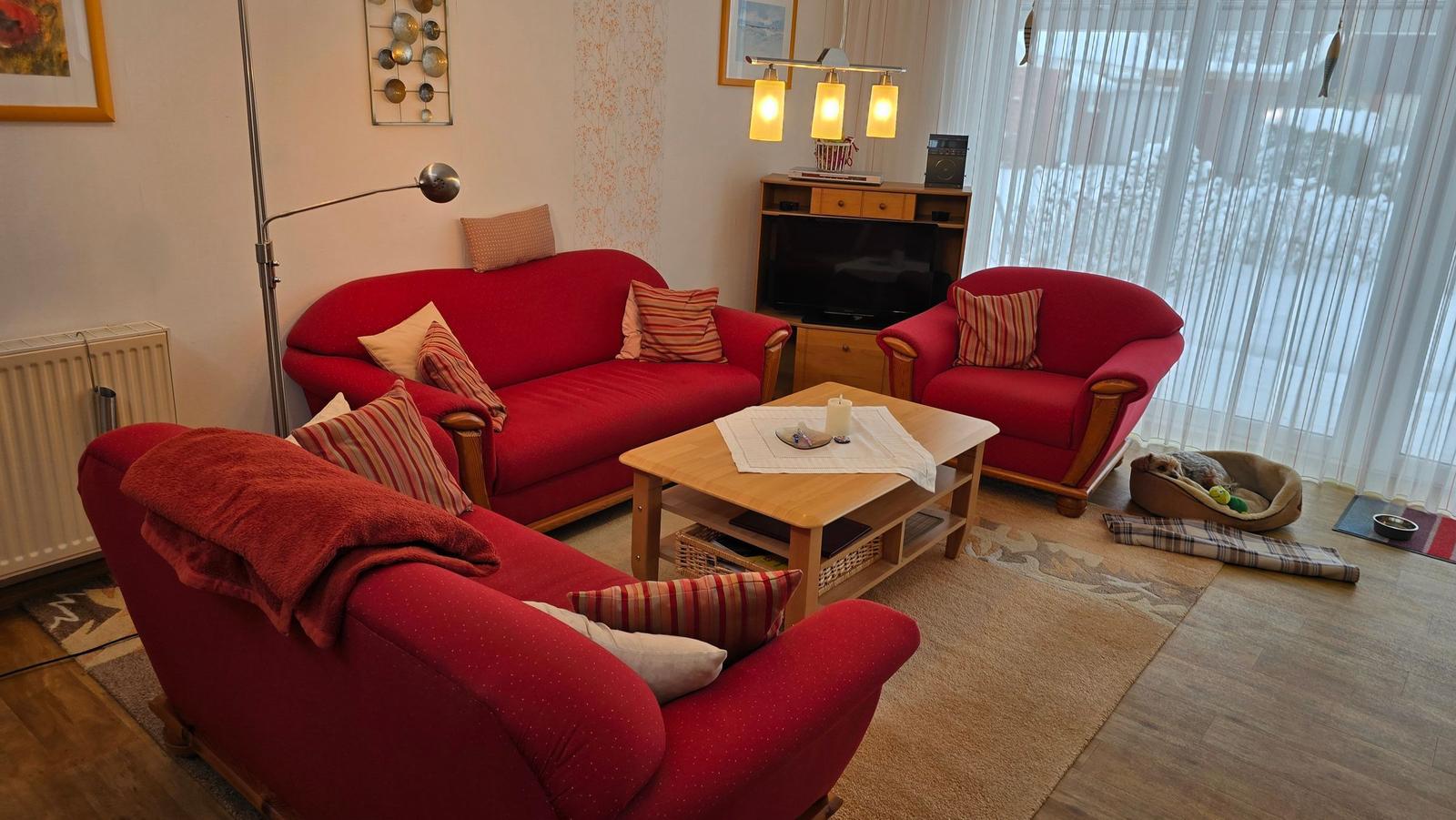 Ein Wohnzimmer mit roten Sesseln, einem Holztisch und einem Fernseher.