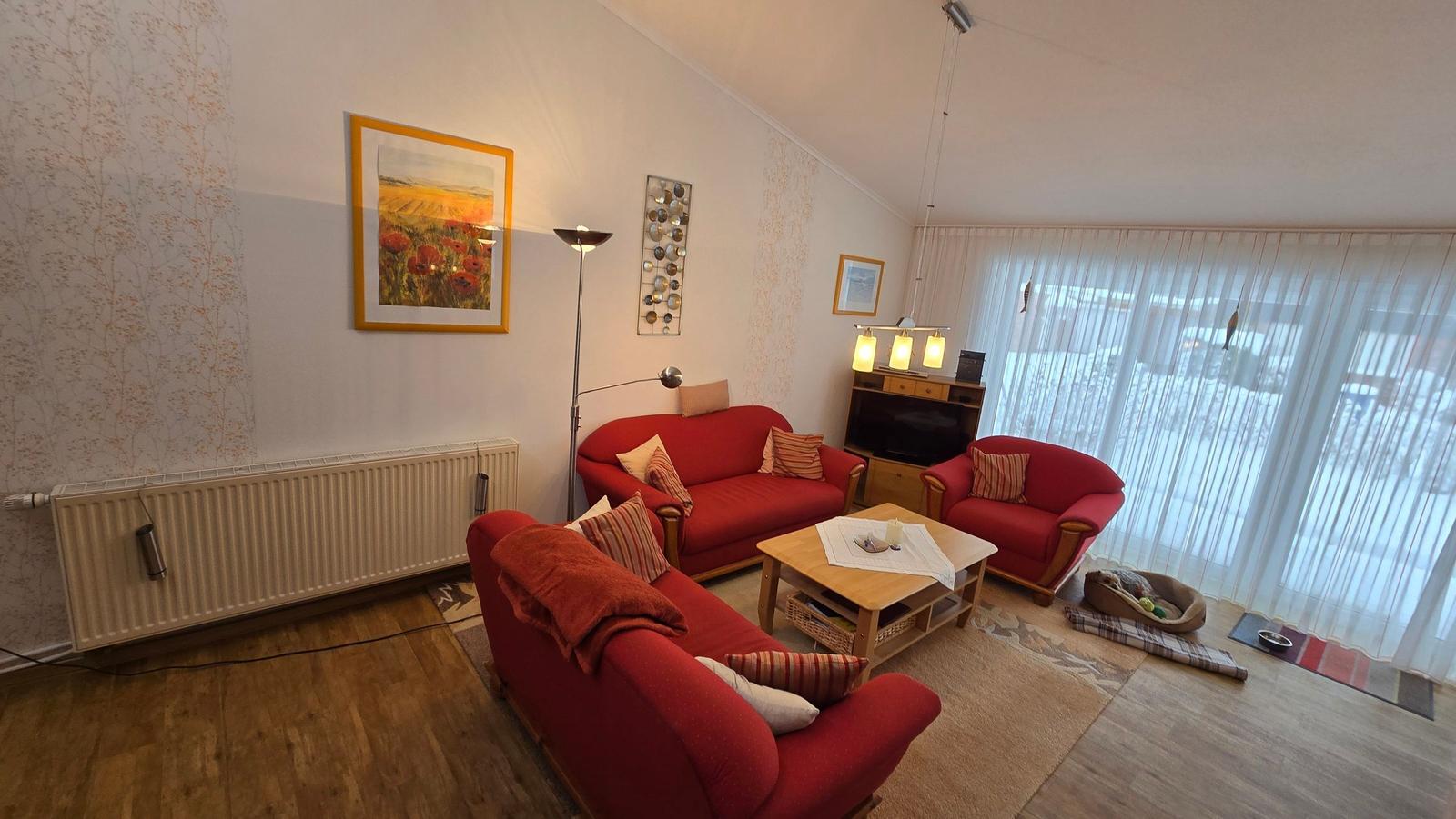 Wohnzimmer mit roten Sofas, Holztisch und großen Fenstern.