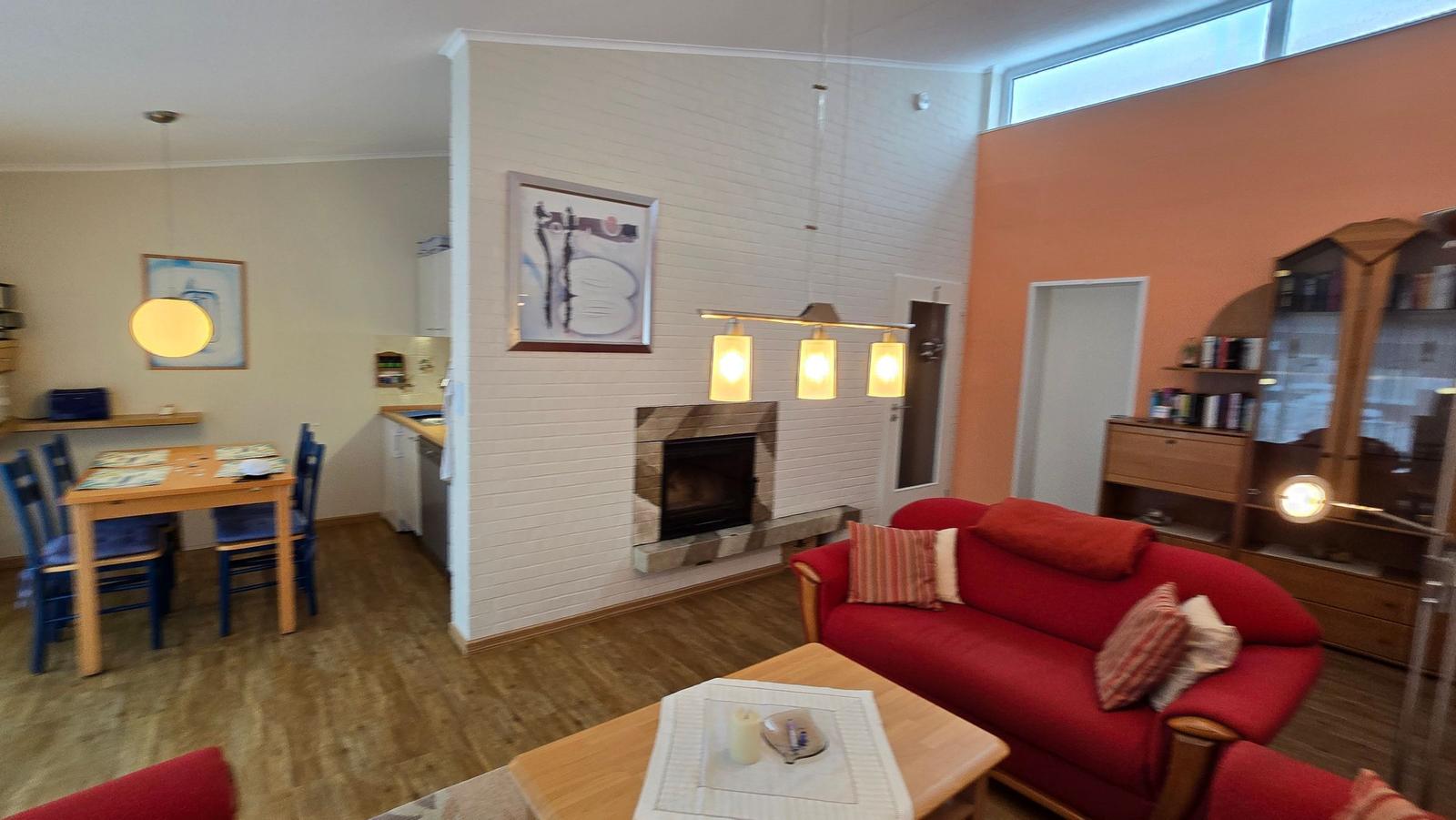 Wohnzimmer mit rotem Sofa, Kamin und Essbereich im Hintergrund.